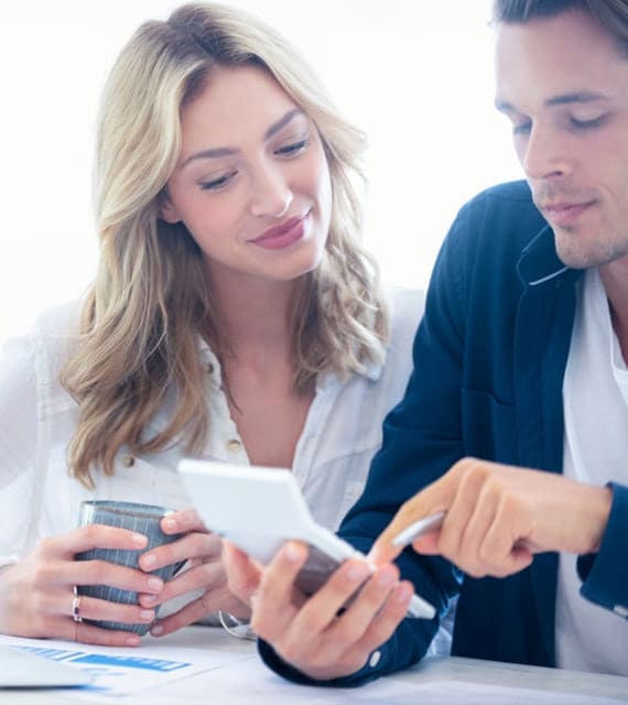 A woman holds a cup while a man points at a document both are reviewing together. They appear focused and engaged in the discussion.