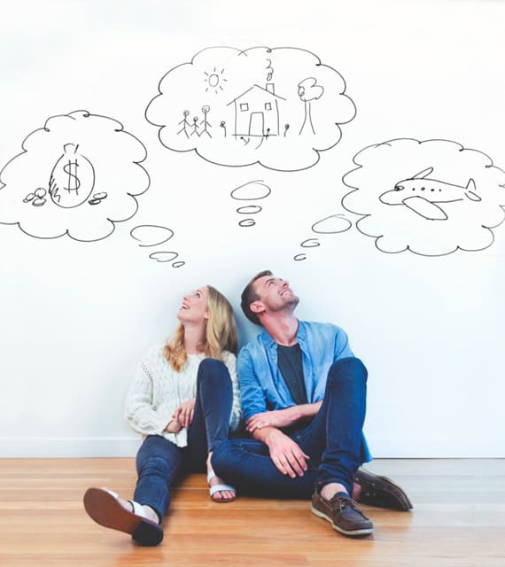 A couple sitting on the floor, looking up, with doodles above their heads depicting money, a house with a family, and an airplane.